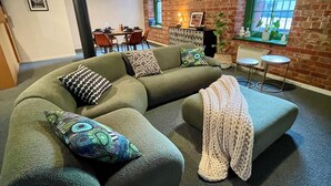 A modern living room with a green sectional sofa, a knitted throw, and a small table with two stools. - Melbourne Riverside Retreat with Pool. Central Location. Family-Friendly. (Southbank)