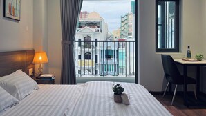 A hotel room with a bed, a desk, a chair, a lamp, and a view of the cityscape. - SenseHome - 5 mins to Bui Vien street  (Ho Chi Minh City)