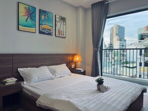 A hotel room with a large bed, a nightstand with a lamp, and a window with a view of the city. - SenseHome - 5 mins to Bui Vien street  (Ho Chi Minh City)