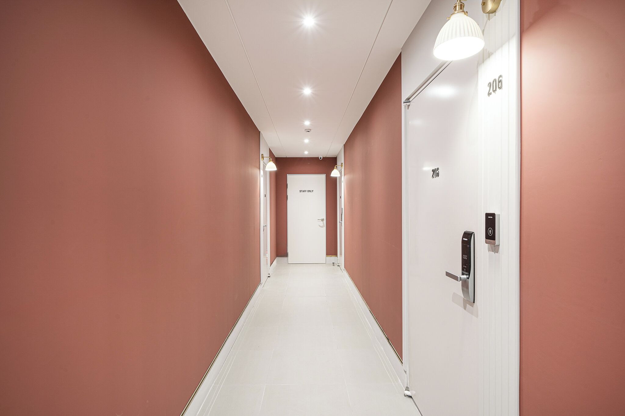 Un pasillo con una puerta blanca que dice 'STAFF ONLY' y el número 206, que da a una habitación.