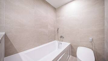 A modern bathroom with a bathtub, toilet, and shower.