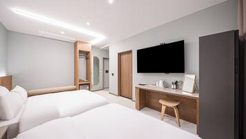 Una habitación de hotel moderna con dos camas, un escritorio, un televisor y un refrigerador.