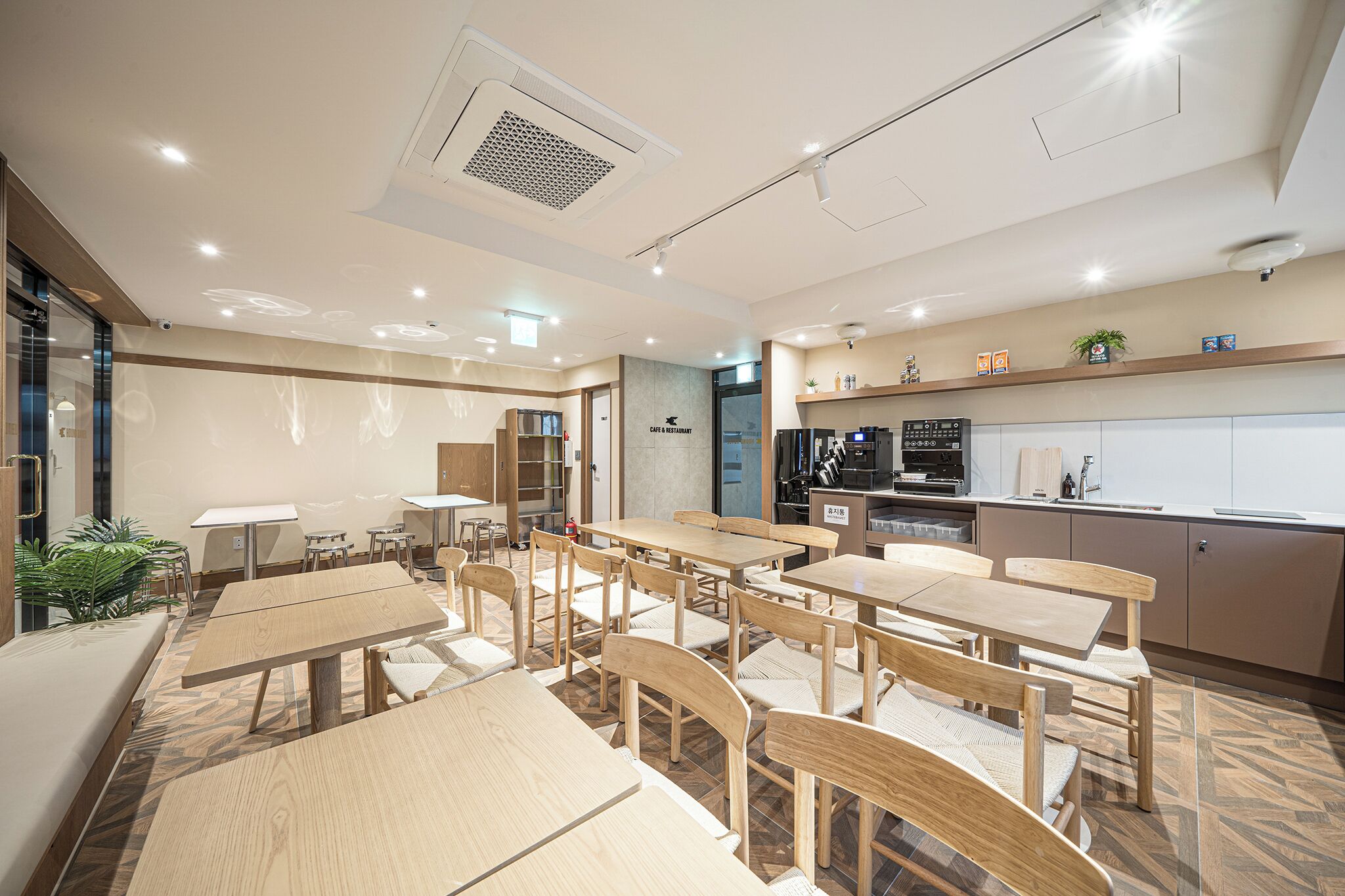 Un café moderno con mesas y sillas de madera, una zona de cocina y un área de estar con un sofá.