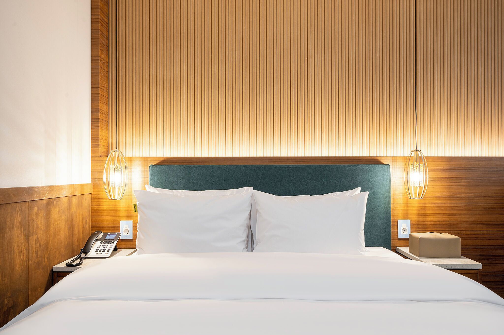 A hotel room with a wooden headboard, a bedside telephone, and a nightstand with a lamp.