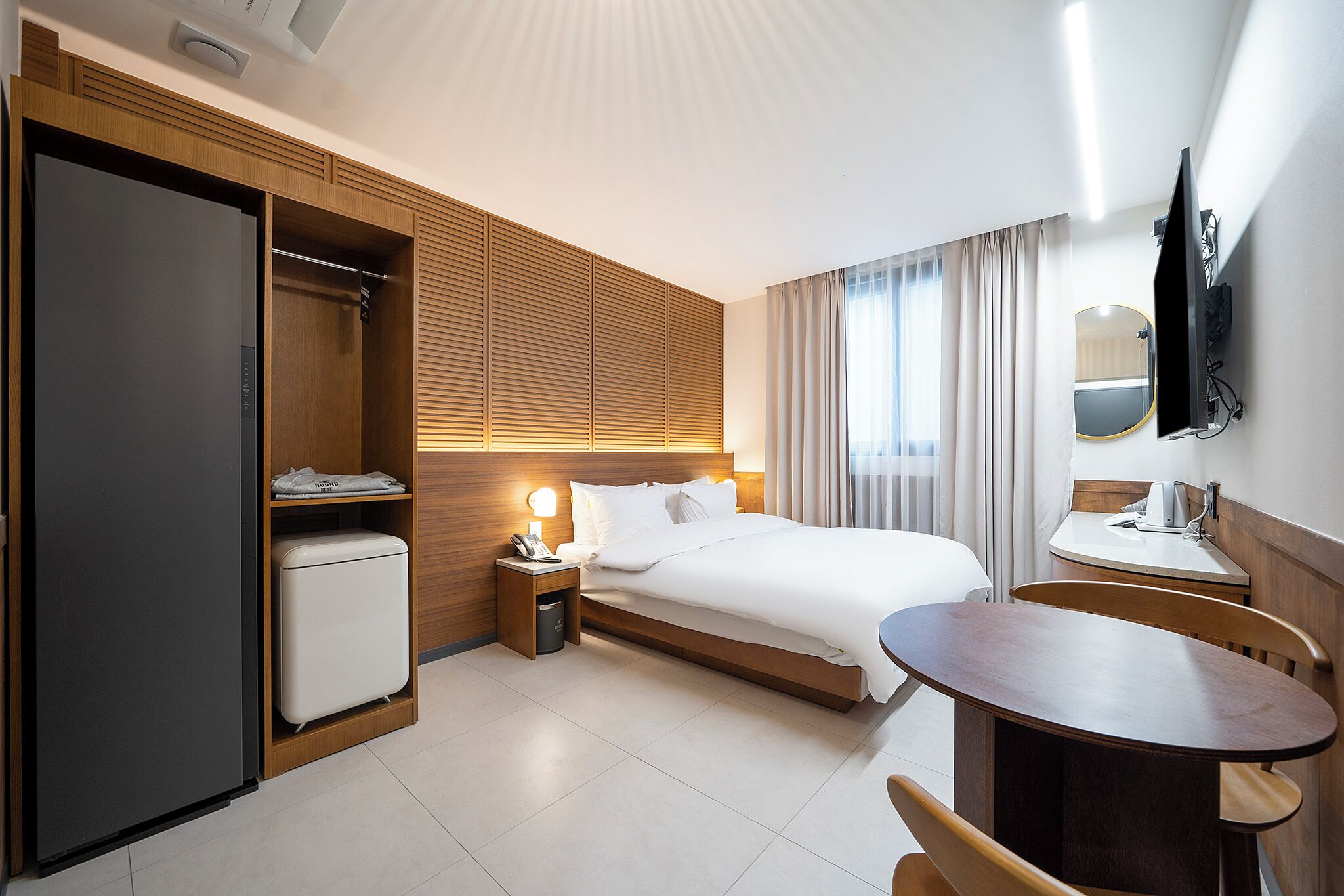 Una habitación de hotel con cama, mesita de noche, lámpara, armario y una pequeña mesa de comedor con sillas.