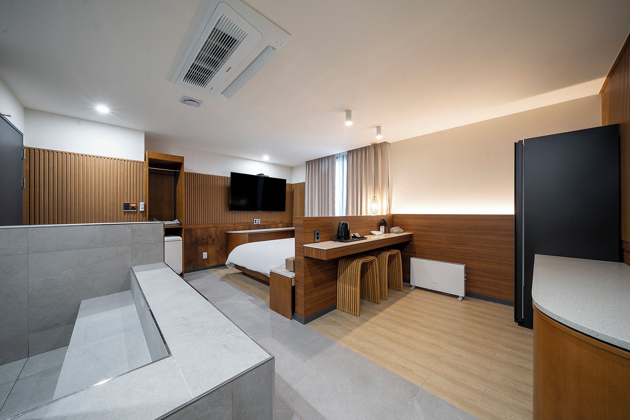 A modern hotel room with a bed, a desk, a TV, and a kitchenette.