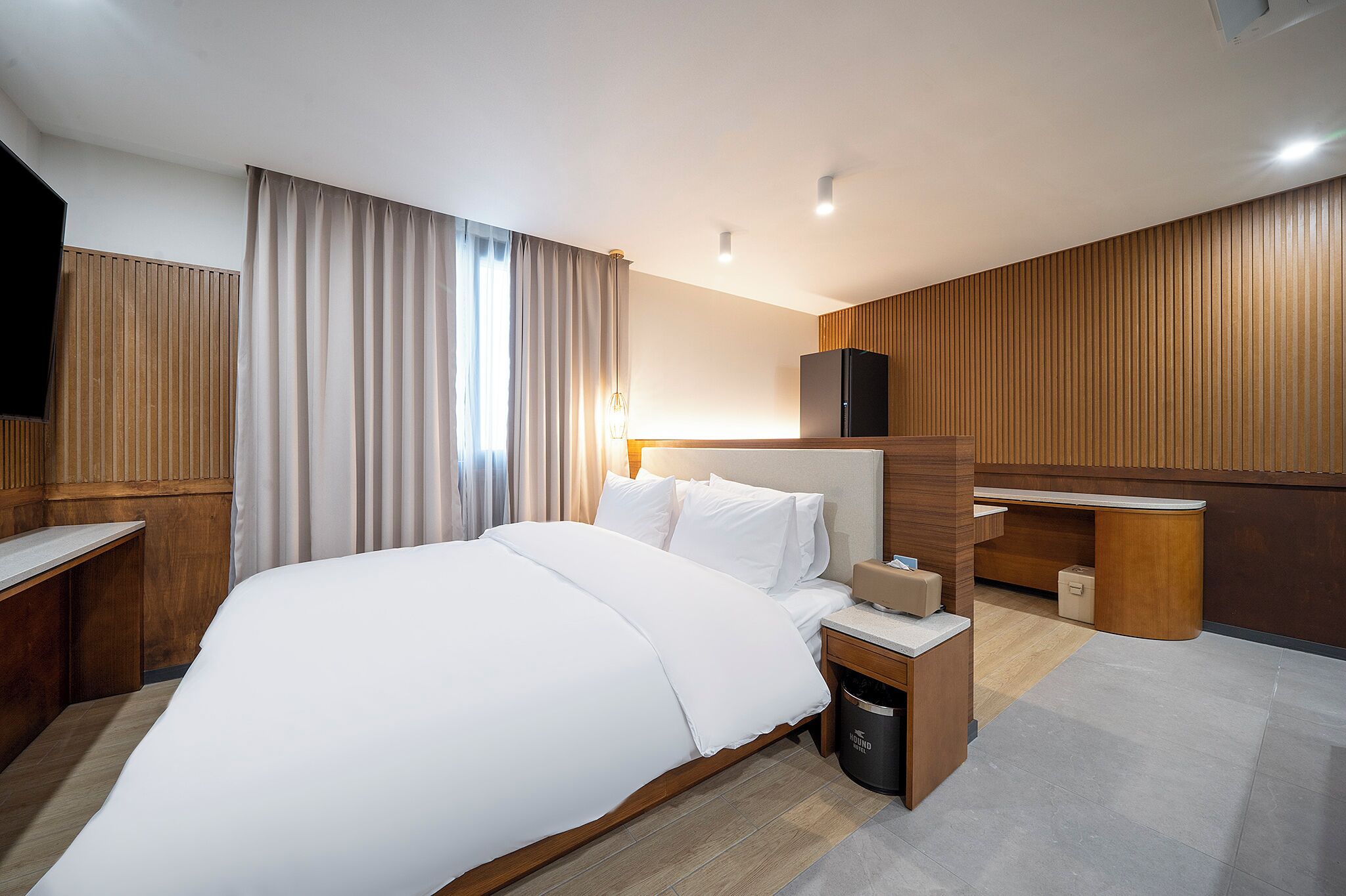 Una habitación de hotel moderna con una cama grande, paneles de madera, un escritorio y un minibar.