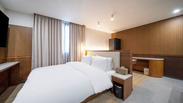 Una habitación de hotel moderna con una cama grande, paneles de madera, un escritorio y un minibar.
