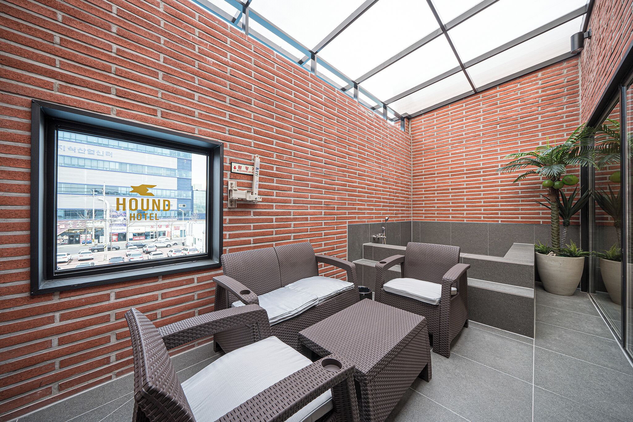 Zona de estar al aire libre con paredes de ladrillo, muebles de mimbre y vista a un edificio de hotel.