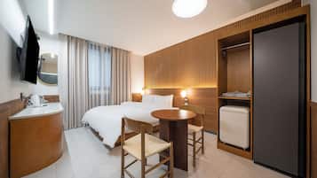 Habitación de hotel con cama, mesita de noche, sillas, una pequeña mesa, espejo, armario y televisor.