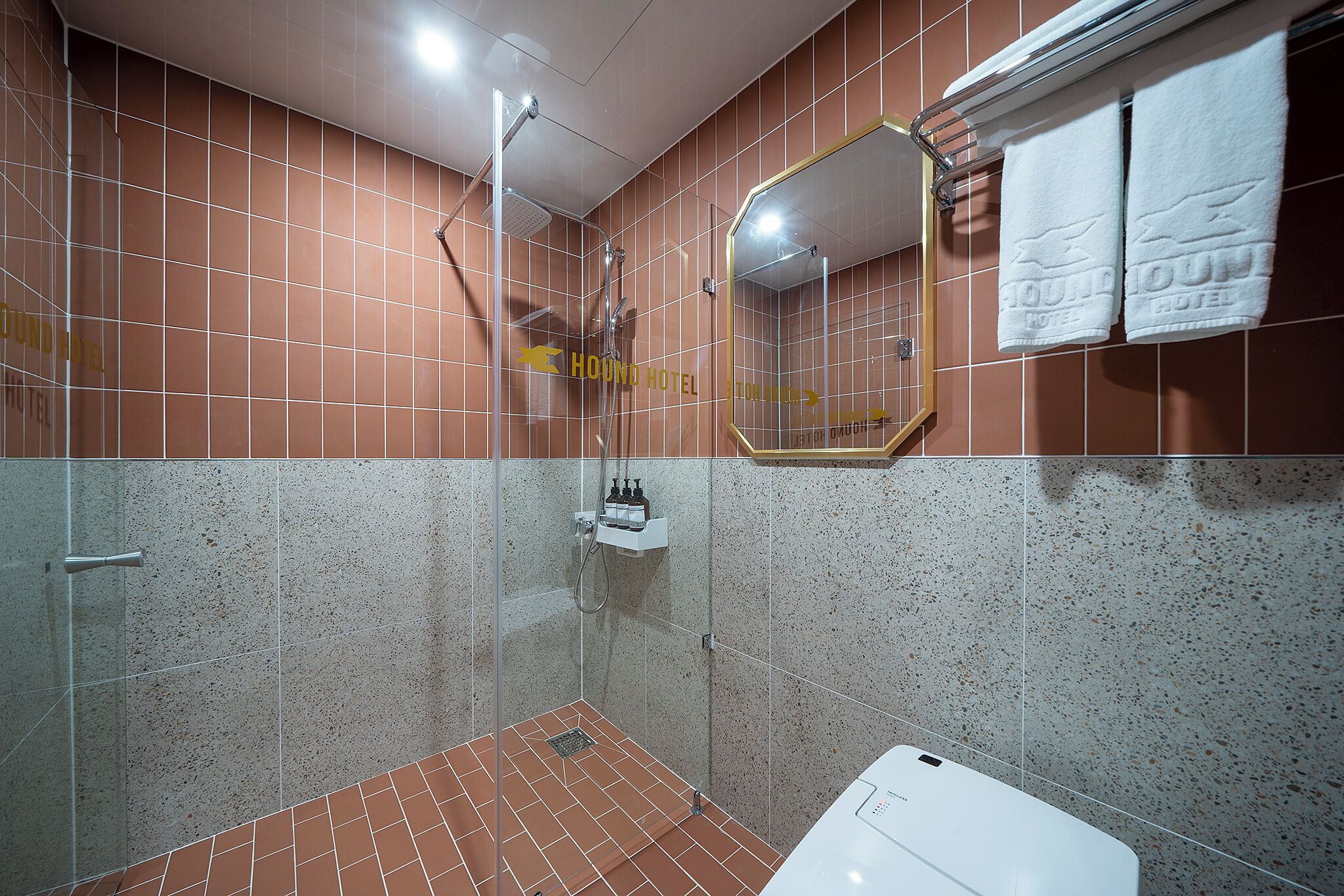 A shower area with a glass door, a white sink, and a mirror with a towel hanging on it.