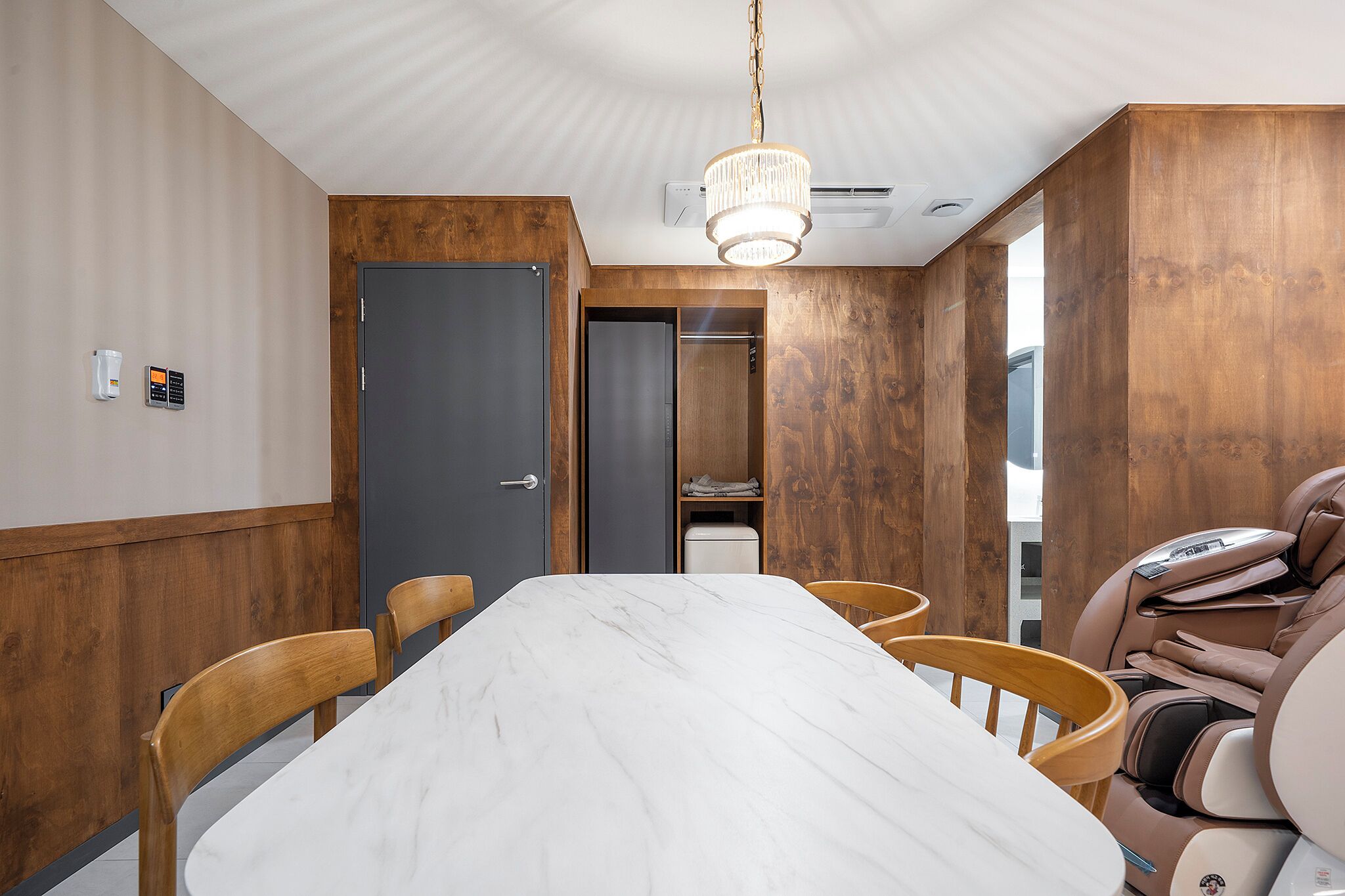 Un salón de conferencias con una mesa de mármol, sillas de madera, un sillón de masaje y un panel de pared de madera.