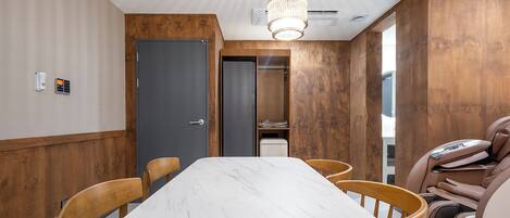 Ein Konferenzraum mit einem Marmortisch, Holzstühlen, einem Massagesessel und einer Wand aus Holzpaneelen.