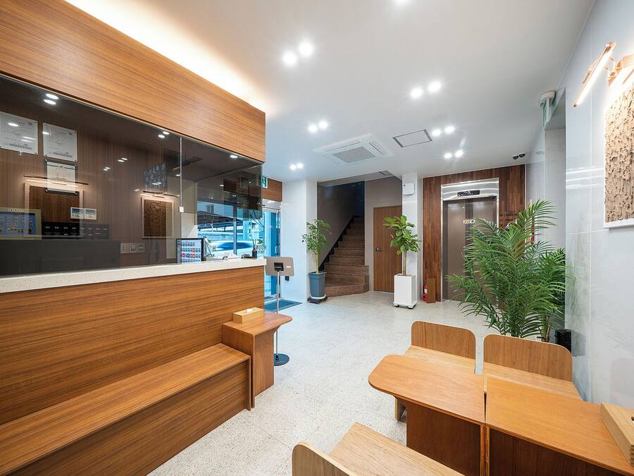 A modern reception area with wooden paneling, a reception desk, seating area, and a staircase leading to an elevator.