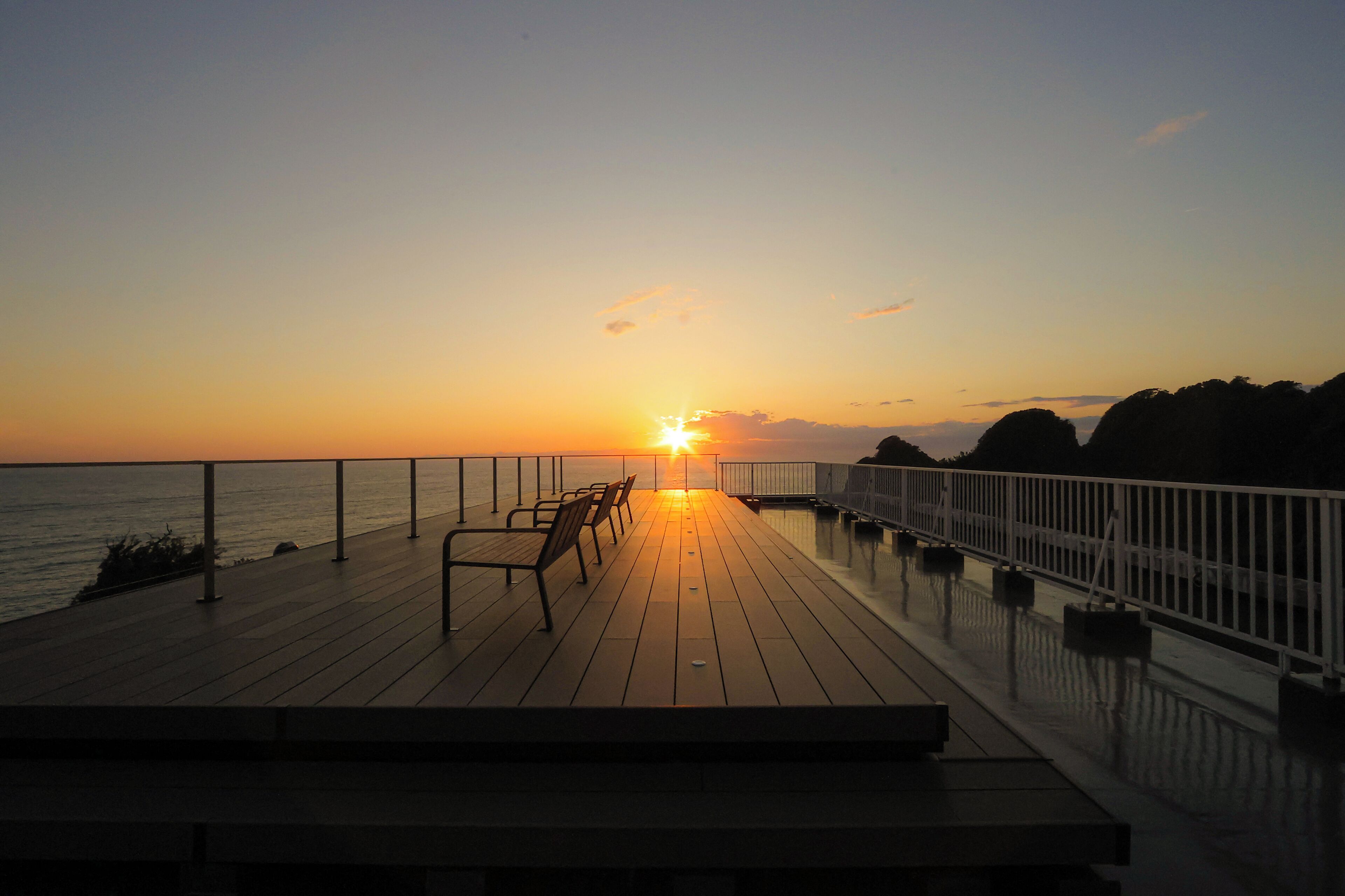 Eine Holzterrasse mit Bänken, die zum Meer hin ausgerichtet sind, bei Sonnenuntergang.