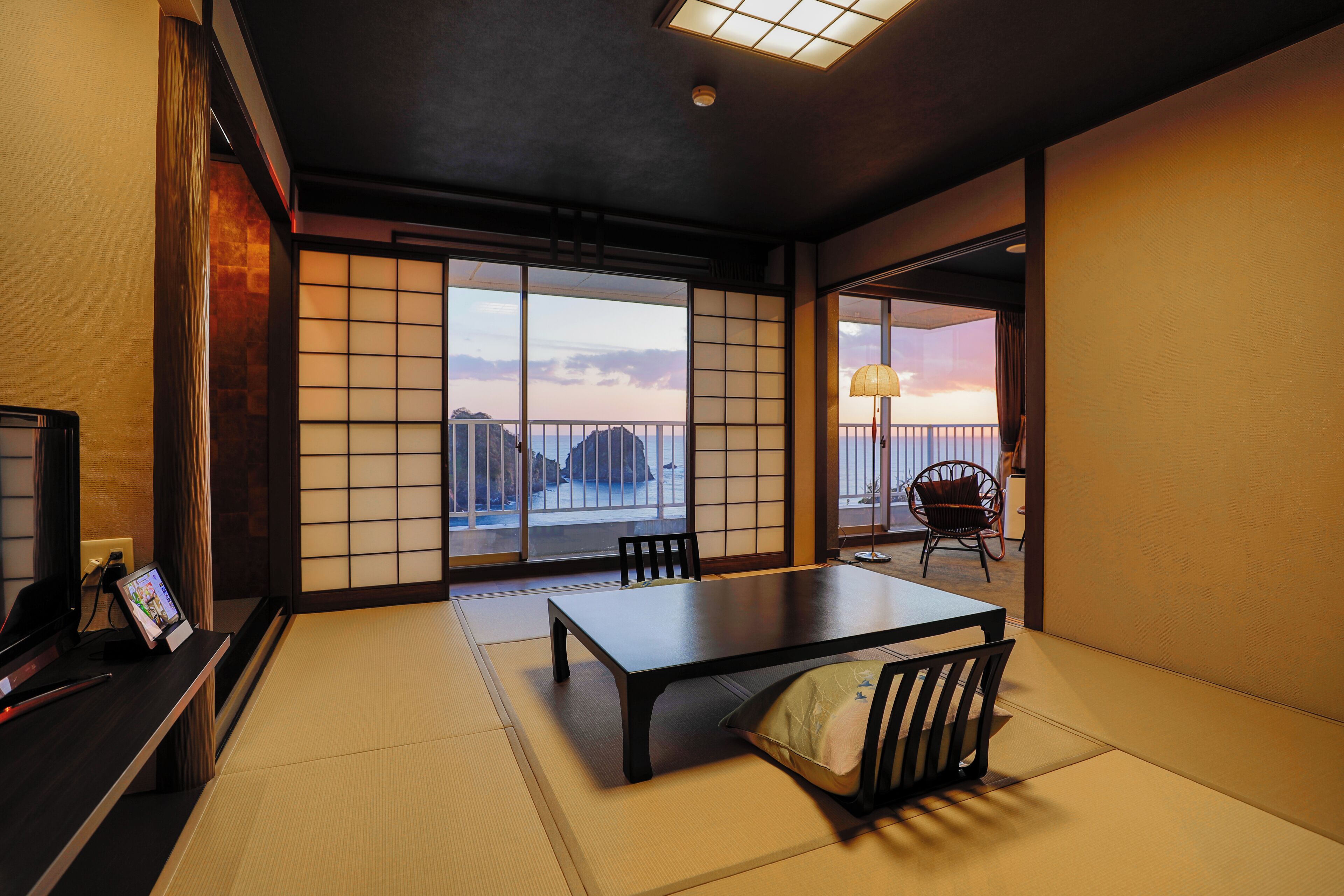 A traditional Japanese room with tatami flooring, a low table, and sliding doors leading to a balcony with a city view.