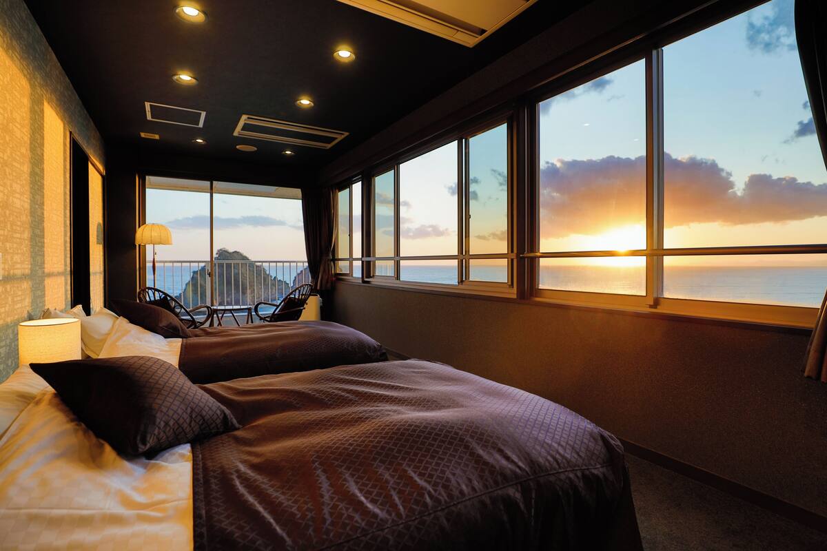Une chambre d’hôtel avec un grand lit, un bureau et une vue sur le coucher de soleil sur l’océan.