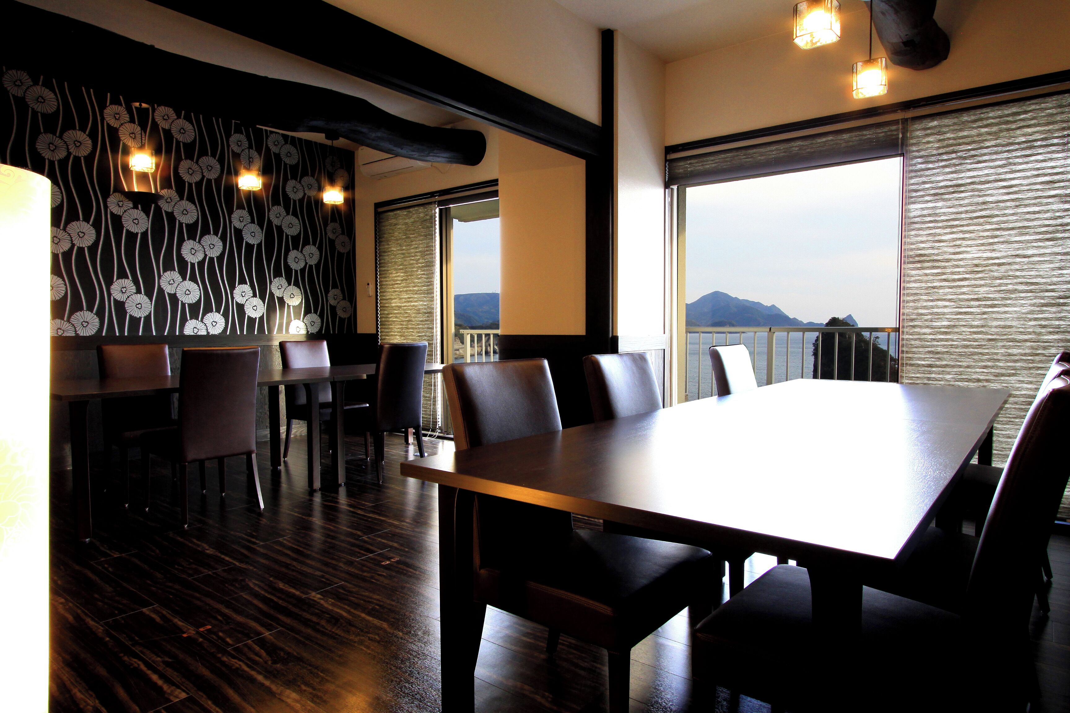 A dining area with a large table and chairs, a patterned wall, and a view of the sea.