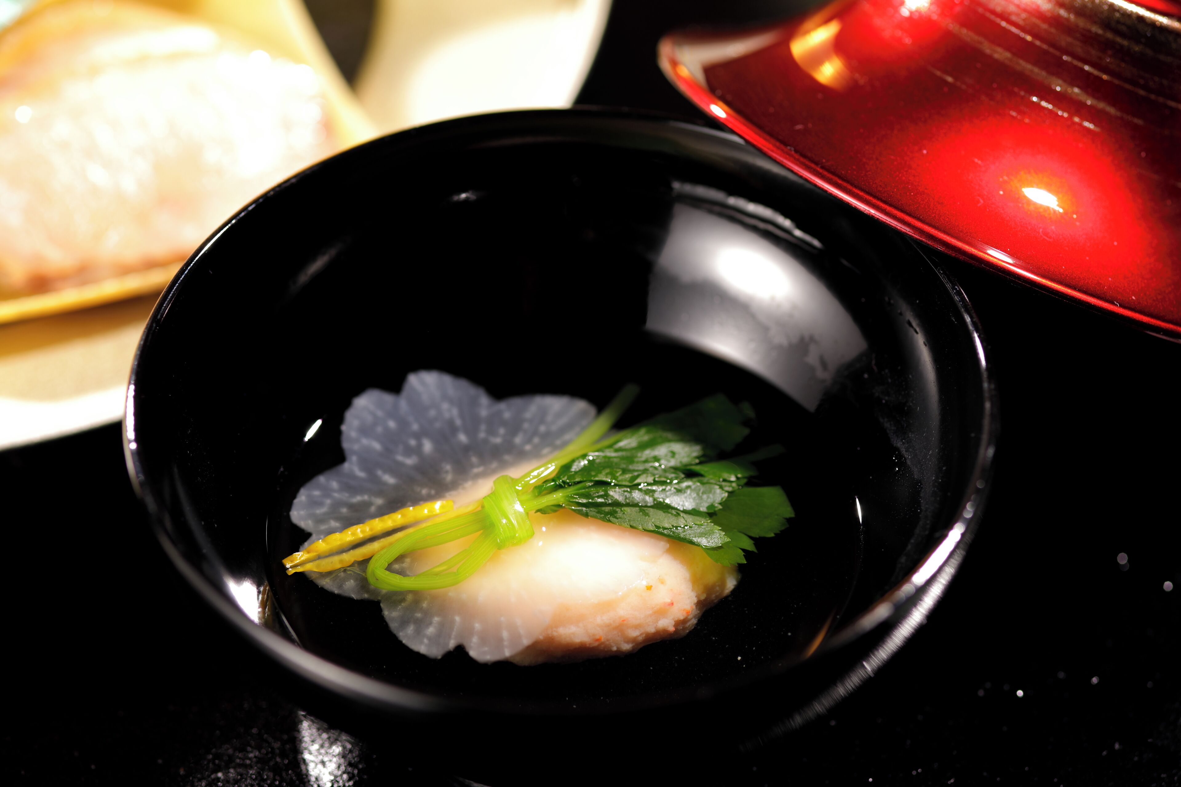 A black bowl with a white fish and green garnish on a black surface.