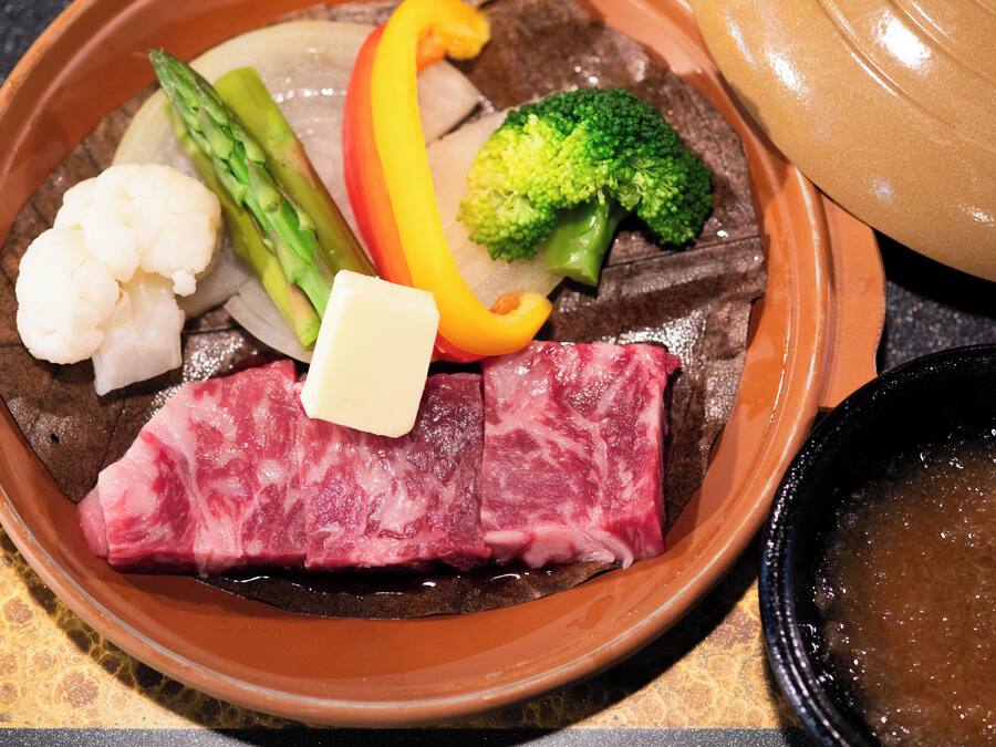 A dish with beef, vegetables, and a small piece of cheese.