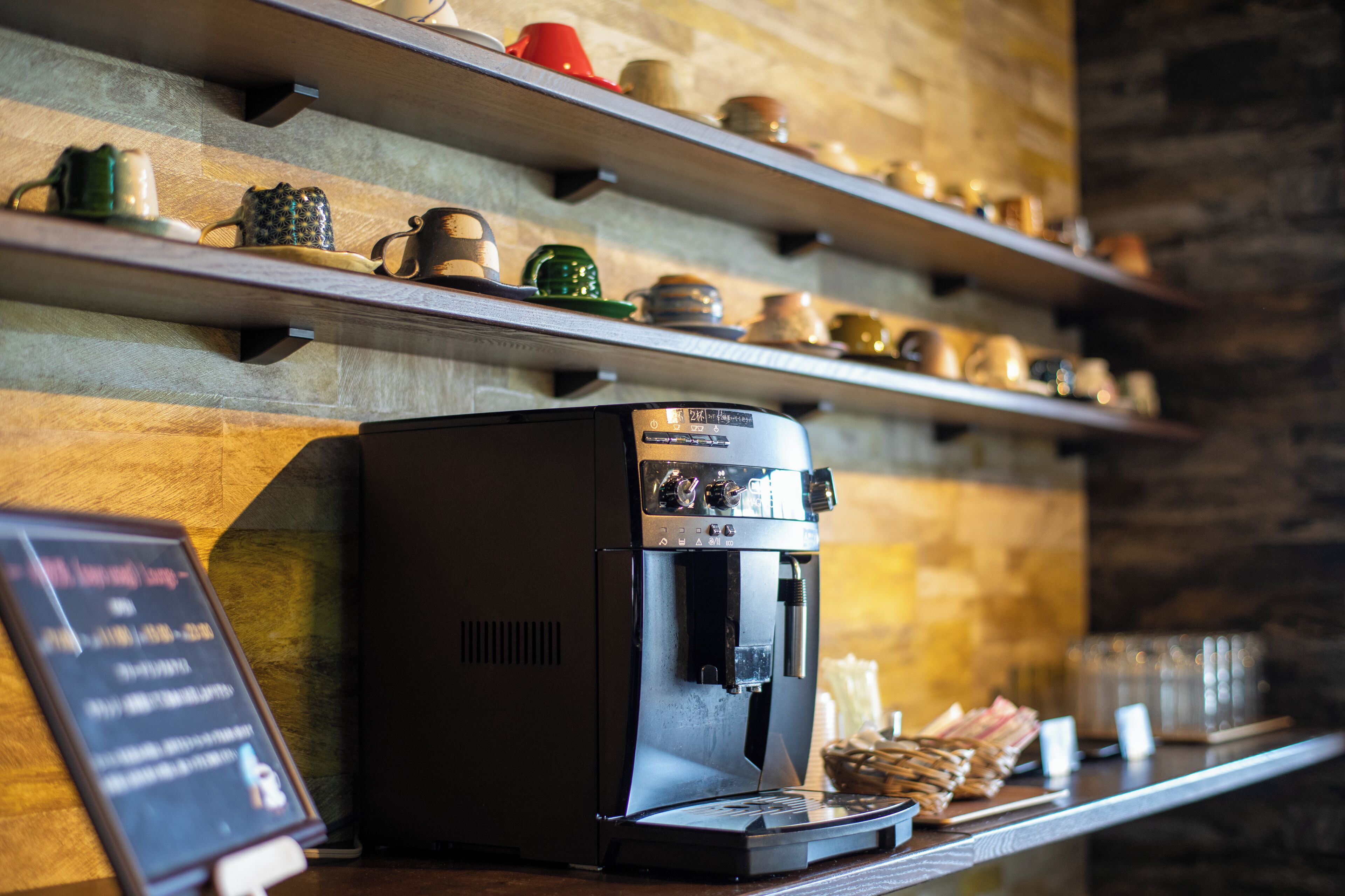 A coffee machine on a counter with shelves above displaying various mugs and teapots.