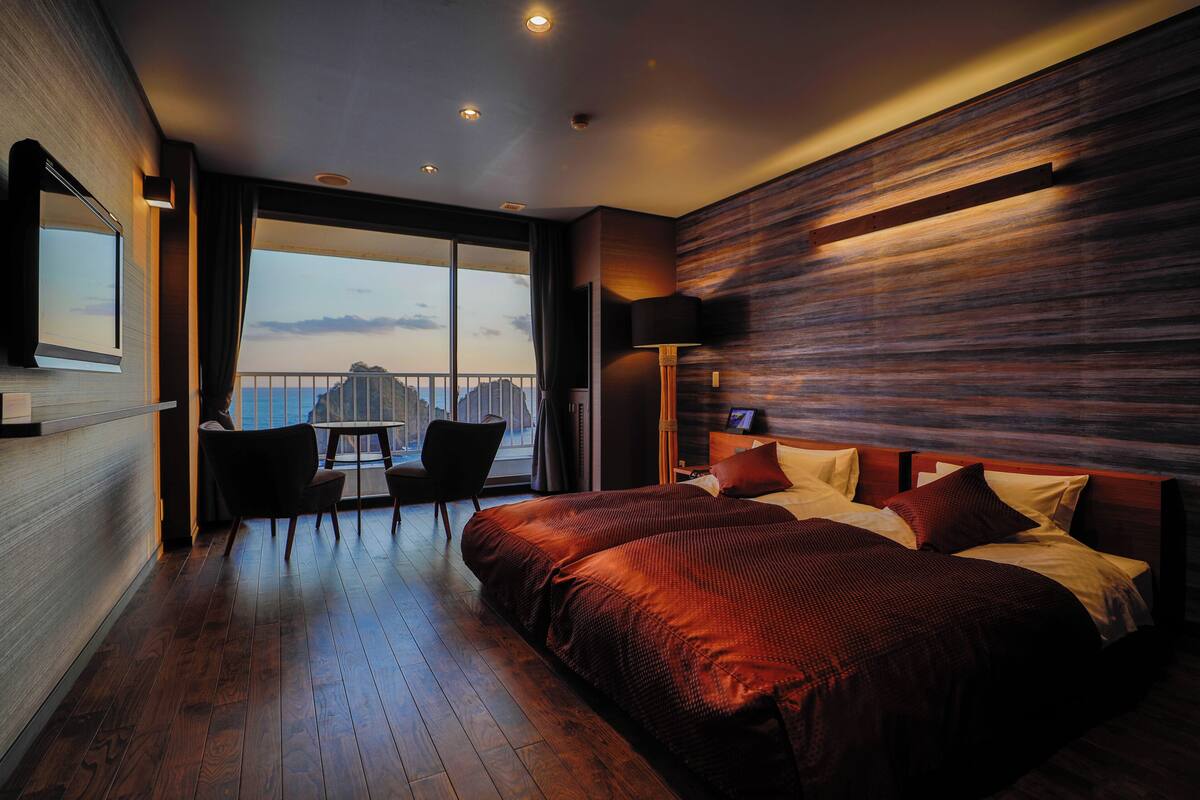 Une chambre d’hôtel moderne dotée d’un grand lit, d’un balcon avec une table et des chaises, et offrant une vue sur la ville.