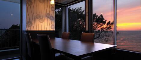 A dining area with a table and chairs, large windows with a view of the sunset, and patterned wallpaper.