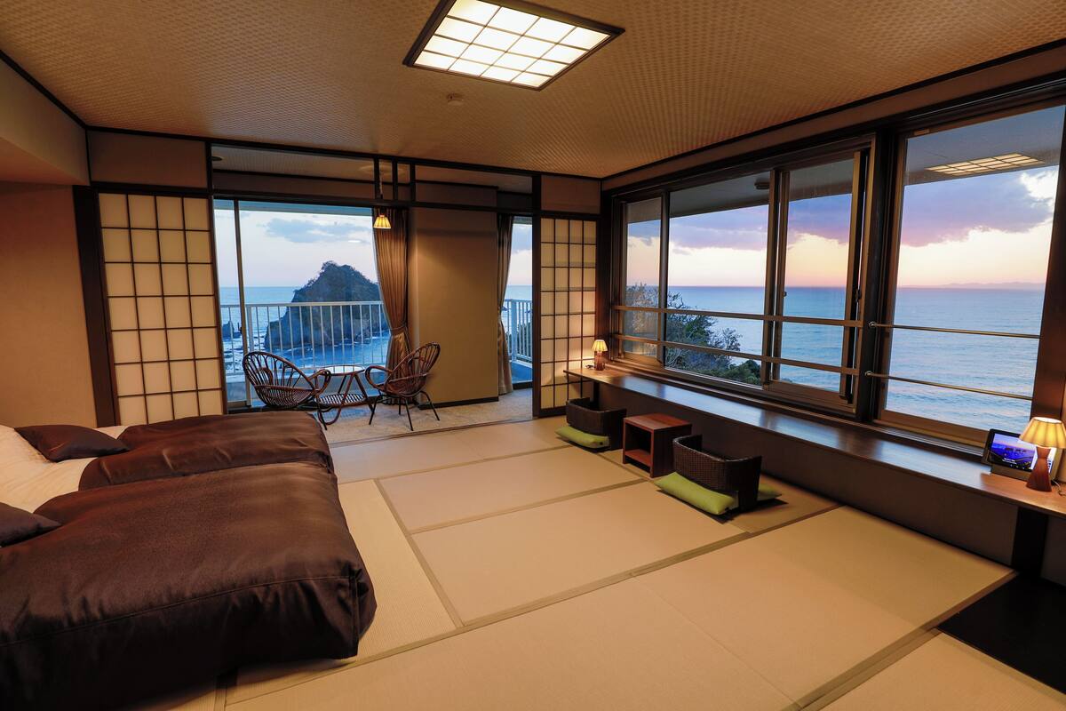 Une pièce de style japonais traditionnel, avec un sol recouvert de tatamis, un canapé, un fauteuil et une vue sur la mer.