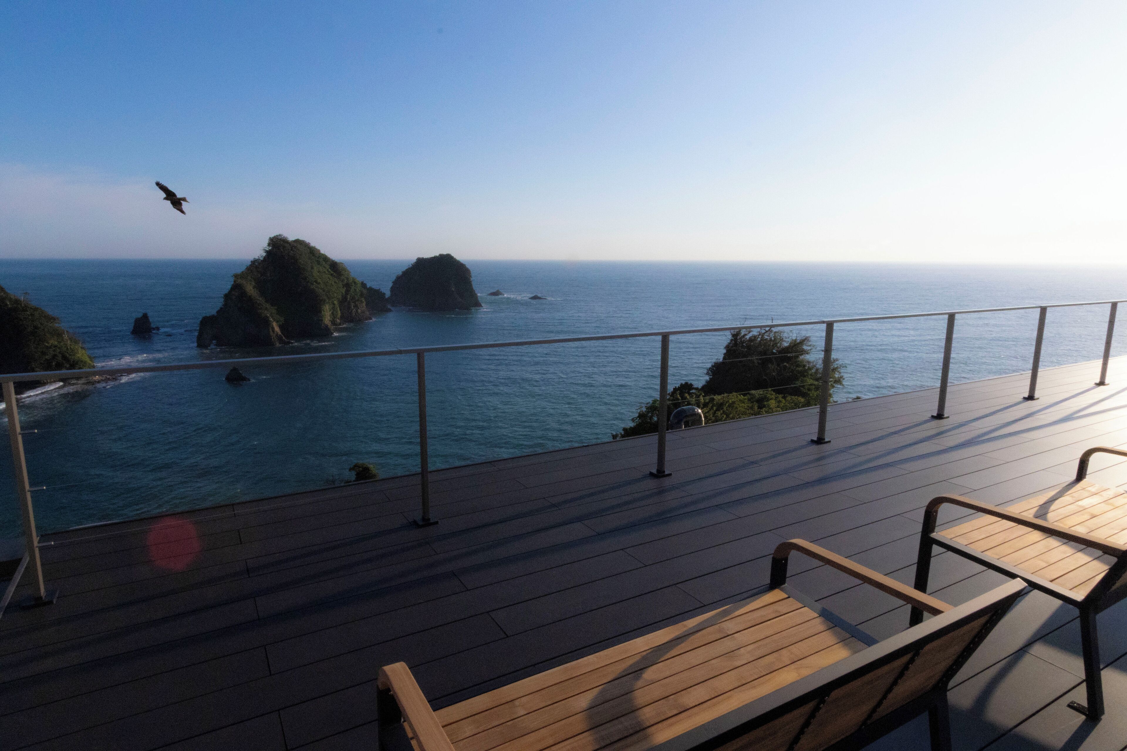 A wooden deck with metal railings overlooking a coastal area with rocky outcrops and the ocean.