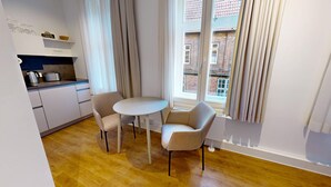 Une cuisine compacte dotée d’appareils électroménagers modernes, un coin repas avec deux chaises et une table, et une fenêtre avec des rideaux.