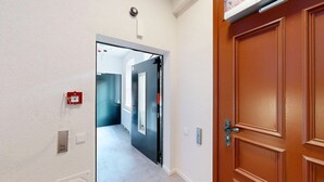 Un couloir avec une porte sur la droite, un détecteur d’incendie sur la gauche et un interrupteur sur le mur.