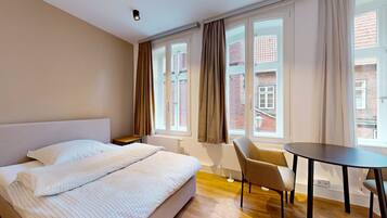 Ein Hotelzimmer mit Bett, Sessel, Tisch und großen Fenstern mit Vorhängen.