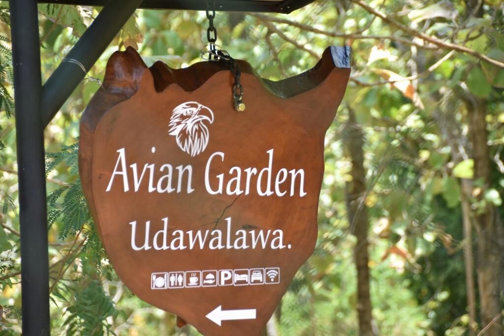 A sign for Avian Garden Udawalawa with directional arrows and symbols indicating amenities.