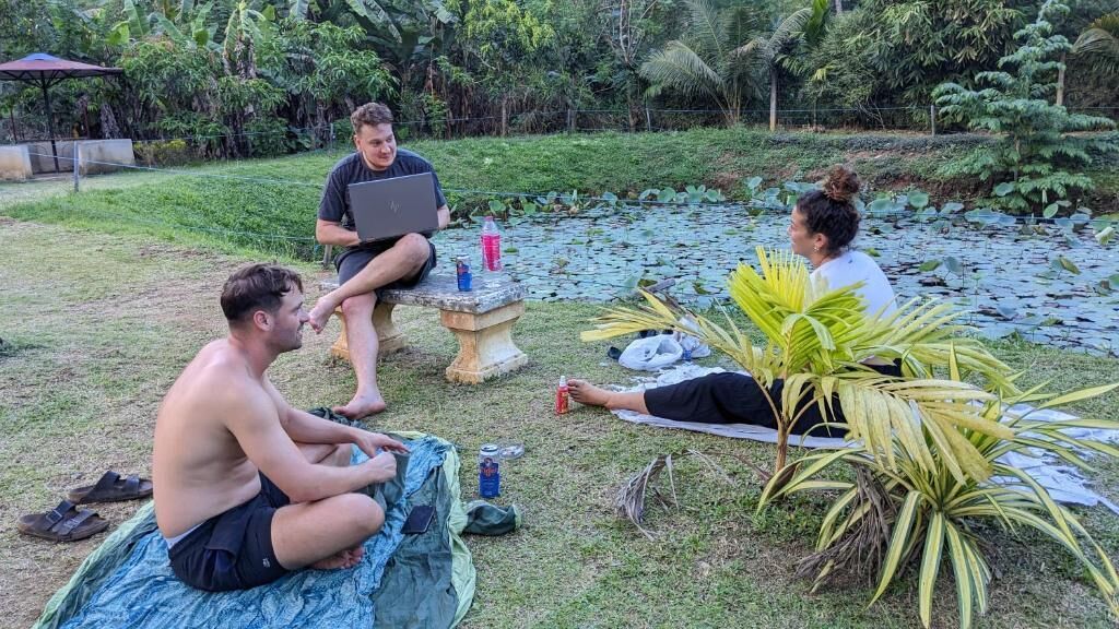 A group of people sitting on a grassy area with a pond in the background.