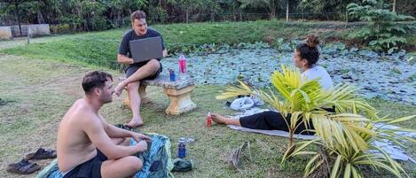 A group of people sitting on a grassy area with a pond in the background.