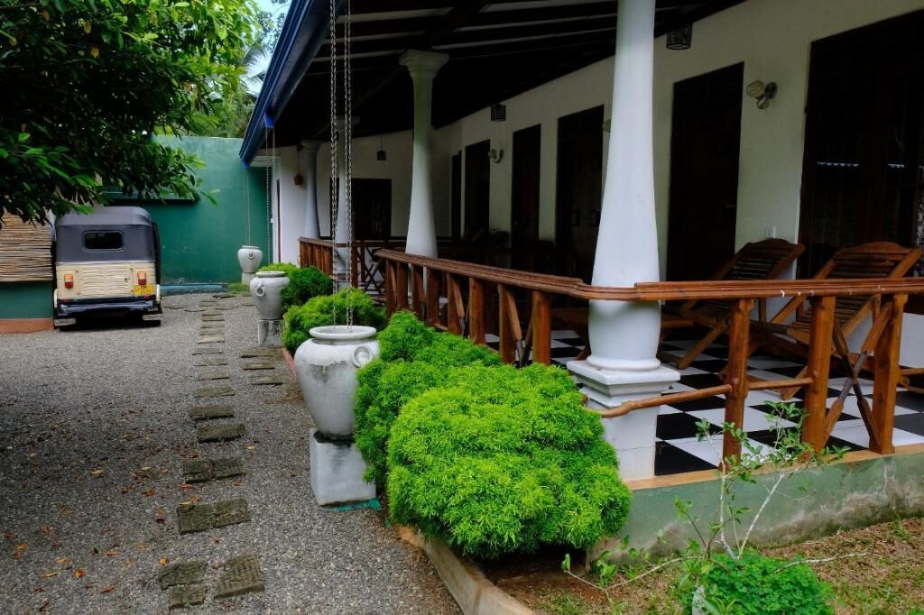 A covered outdoor area with a checkered floor, white columns, and a row of potted plants.