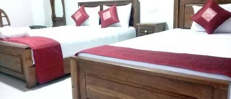 Habitación de hotel con dos camas de madera, cada una con una manta y almohadas rojas.