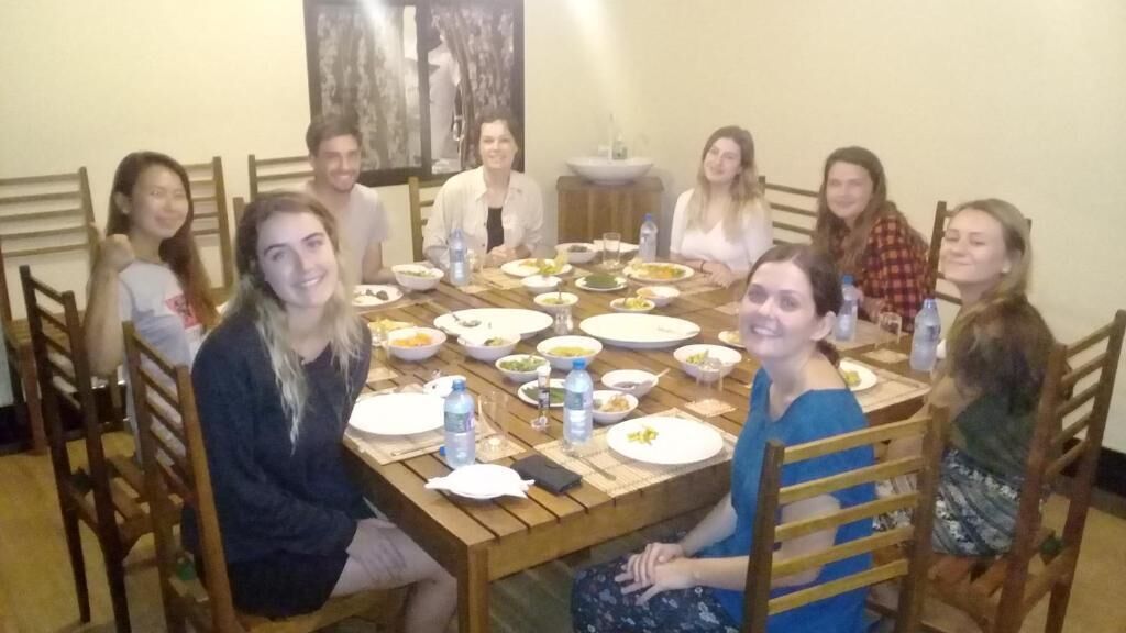 A group of people seated around a wooden dining table with various dishes and drinks.