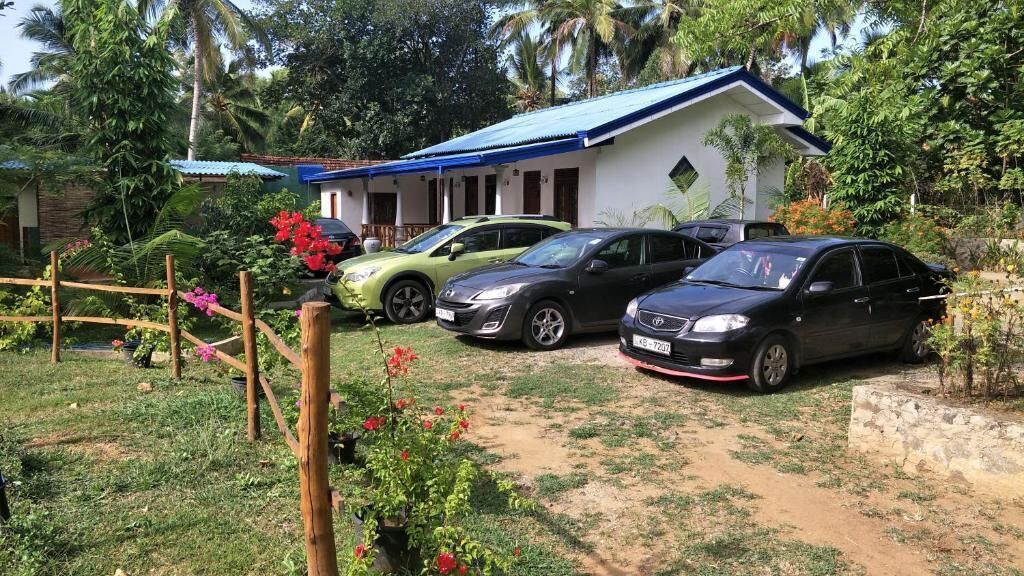 A house with a blue roof, two cars parked in front, and a garden with flowers and trees.