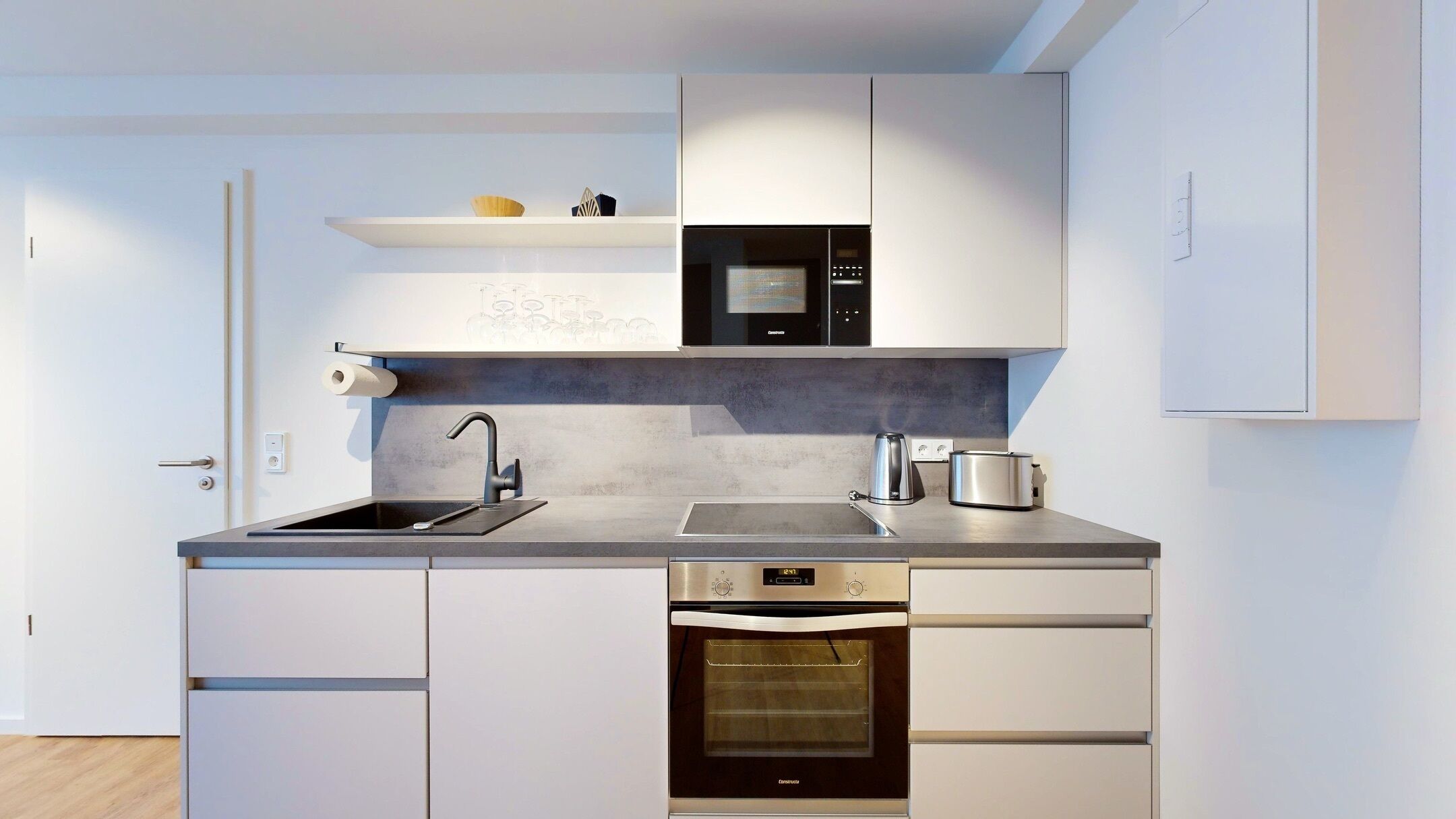 Una cocina moderna con horno empotrado, microondas y cafetera.