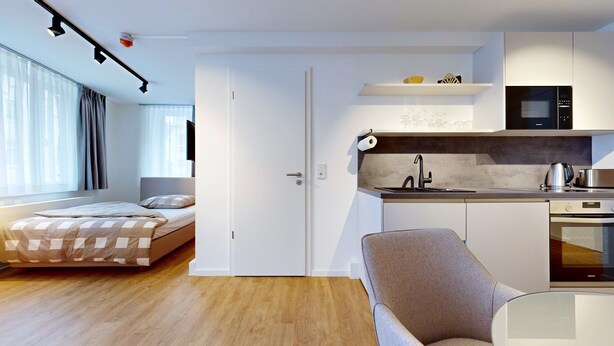 A modern apartment with a kitchenette, a bed, a seating area, and a large window.