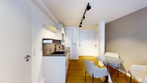 A modern kitchen with a built-in oven, a sink, and a countertop. There is a dining area with a round table and two chairs.
