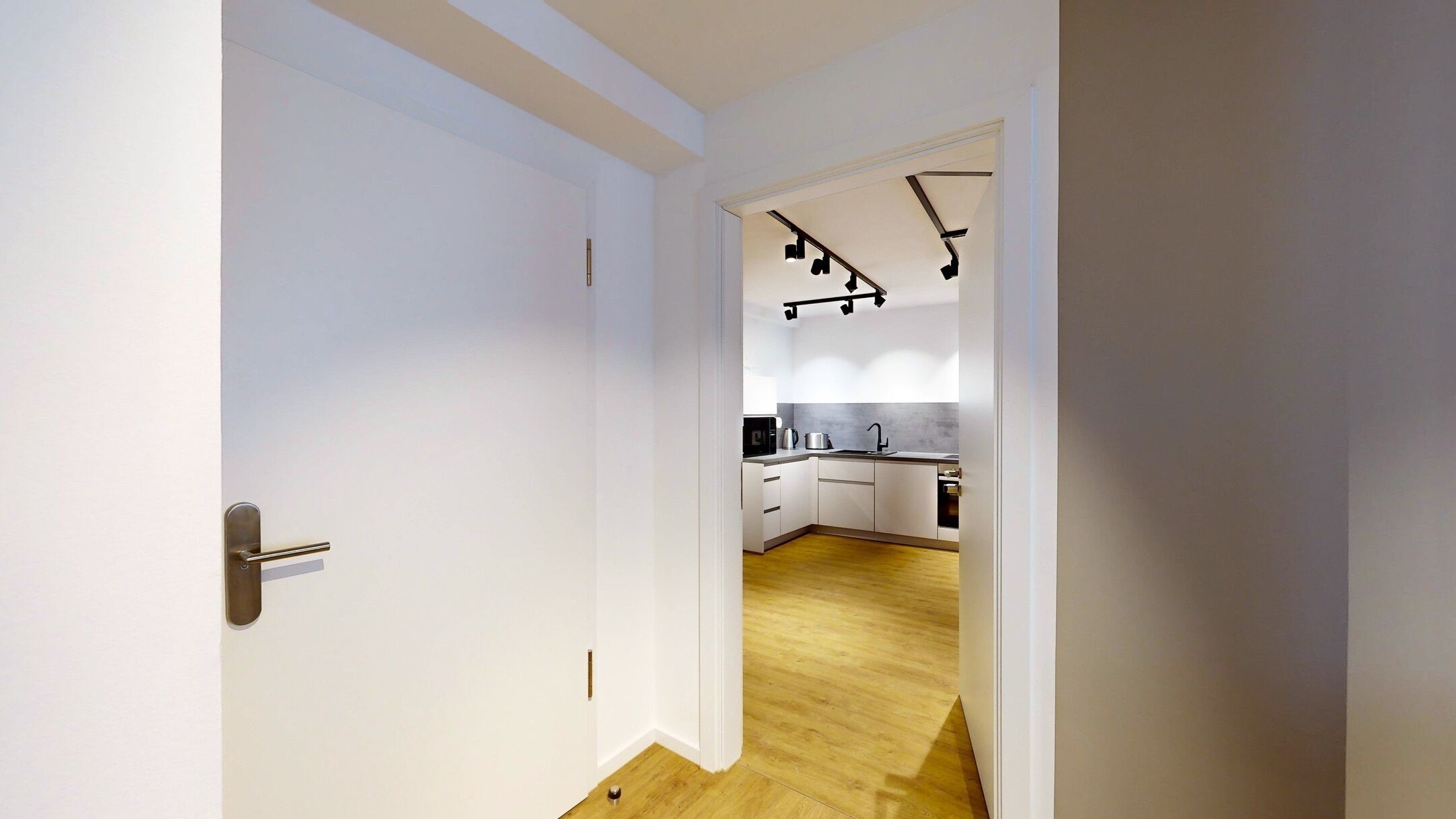 Una cocina moderna con armarios blancos, piso de madera y lámpara de techo negra.