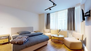Et moderne hotelværelse med seng, et lille bord, en stol og et fjernsyn ophængt på væggen.