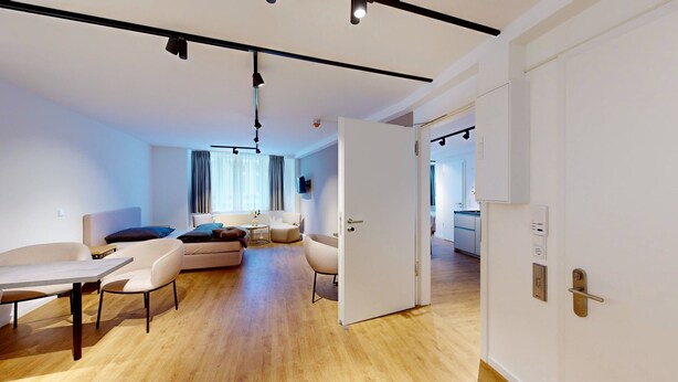 En moderne og lys stue med sofa, stole, spisebord og et stort vindue med gardiner.
