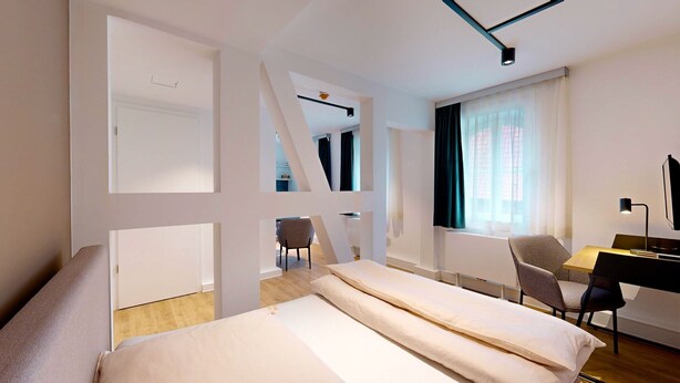 Een moderne hotelkamer met een bed, een bureau met stoel, nog een stoel en een raam met gordijnen.
