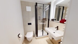 Een moderne badkamer met een douchecabine van glas, een wit toilet en een wastafel met een spiegel erboven.