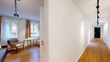 Ein modernes Interieur mit Holzboden, einem runden Tisch, zwei Stühlen, einer Couch und einem Fenster mit Vorhängen.