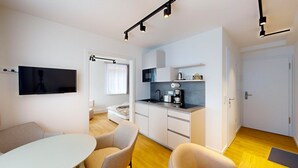 A modern kitchen with a flat-screen TV, a dining area with a round table and chairs, and a separate living space with a sofa and a window. - Apartment 9 | Boardinghouse Lüneburg No8A (Lüneburg)