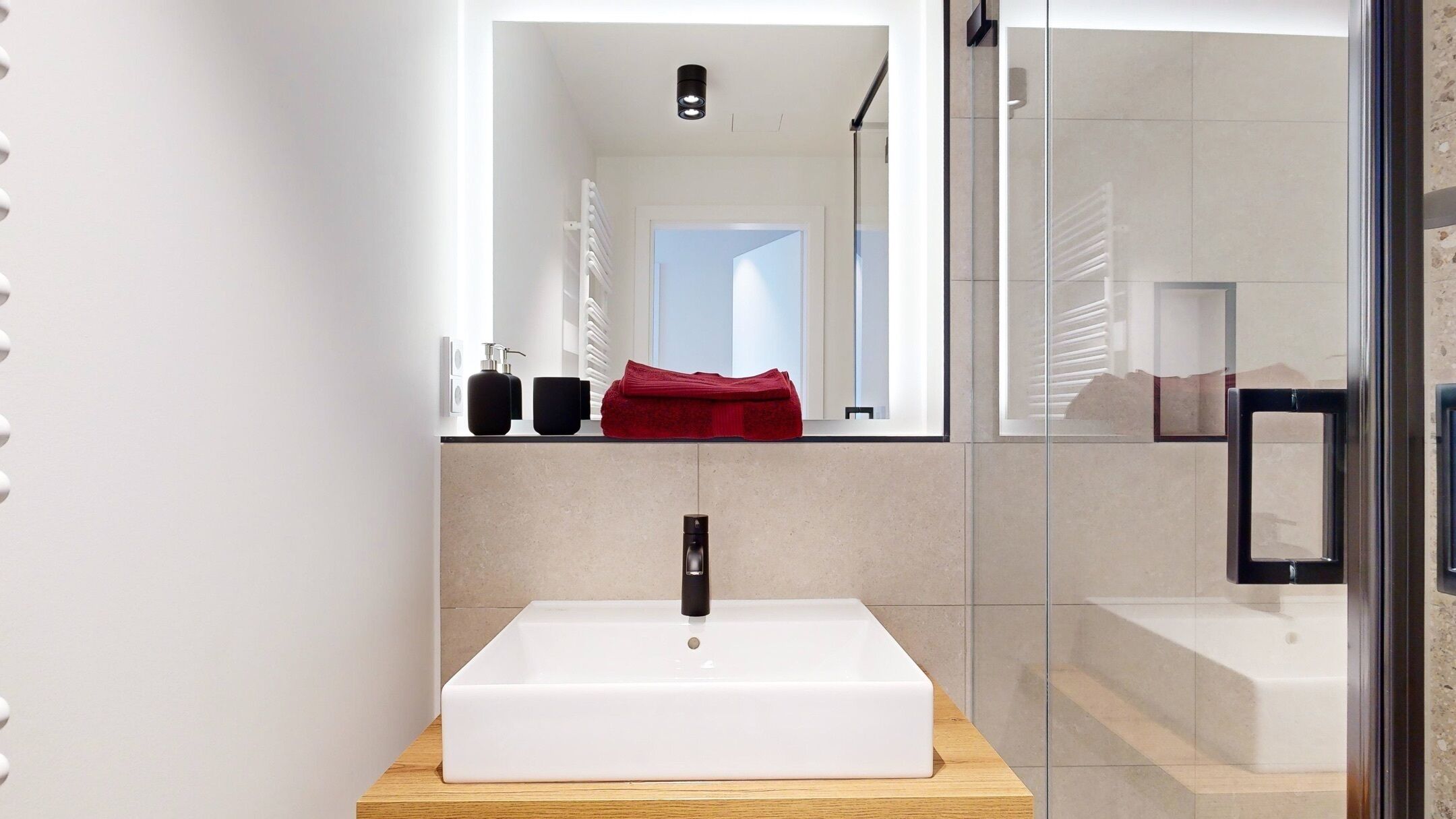 Ein modernes Badezimmer mit Waschbecken, Holztischplatte und Duschkabine aus Glas.